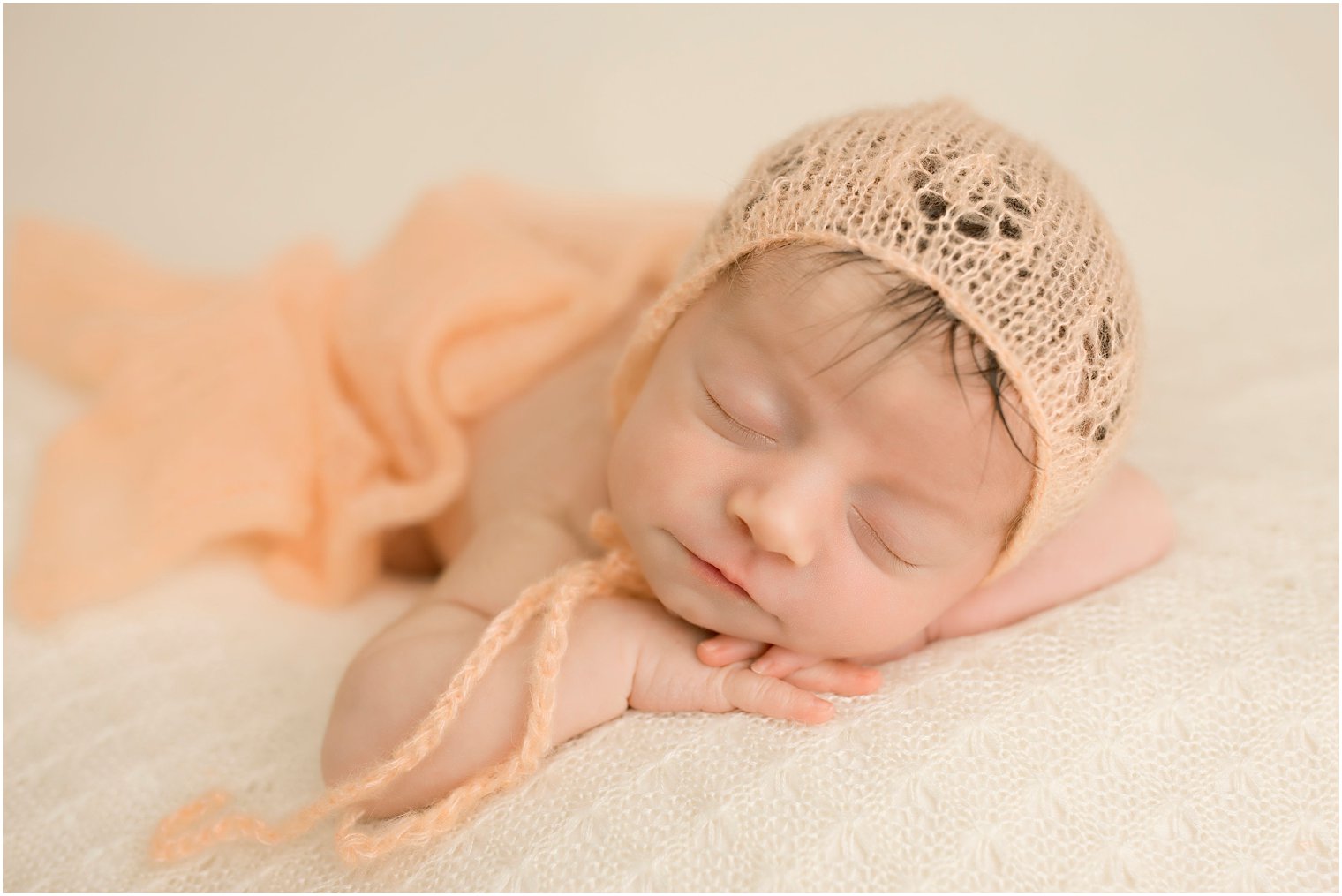 Newborn girl in peach knit bonnet and blanket | Photo by Idalia Photography