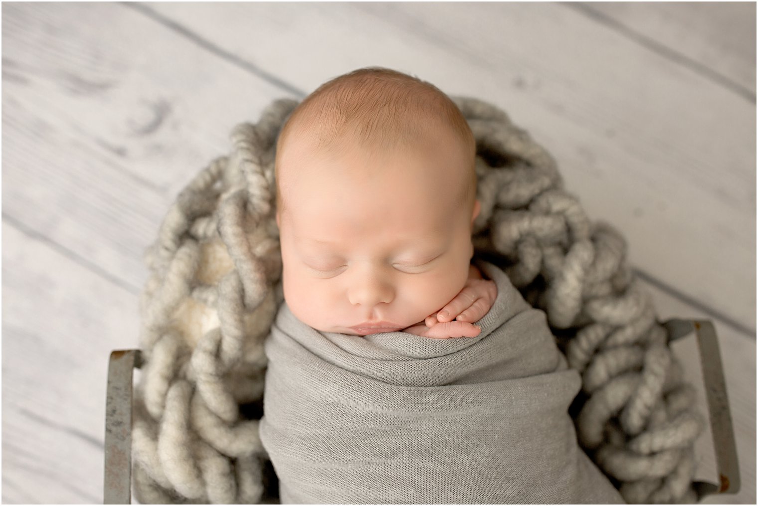 Newborn boy in gray blanket and wire basket