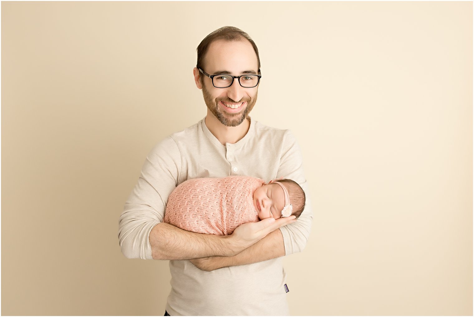 Father wearing cream shirt holding baby swaddled in pink