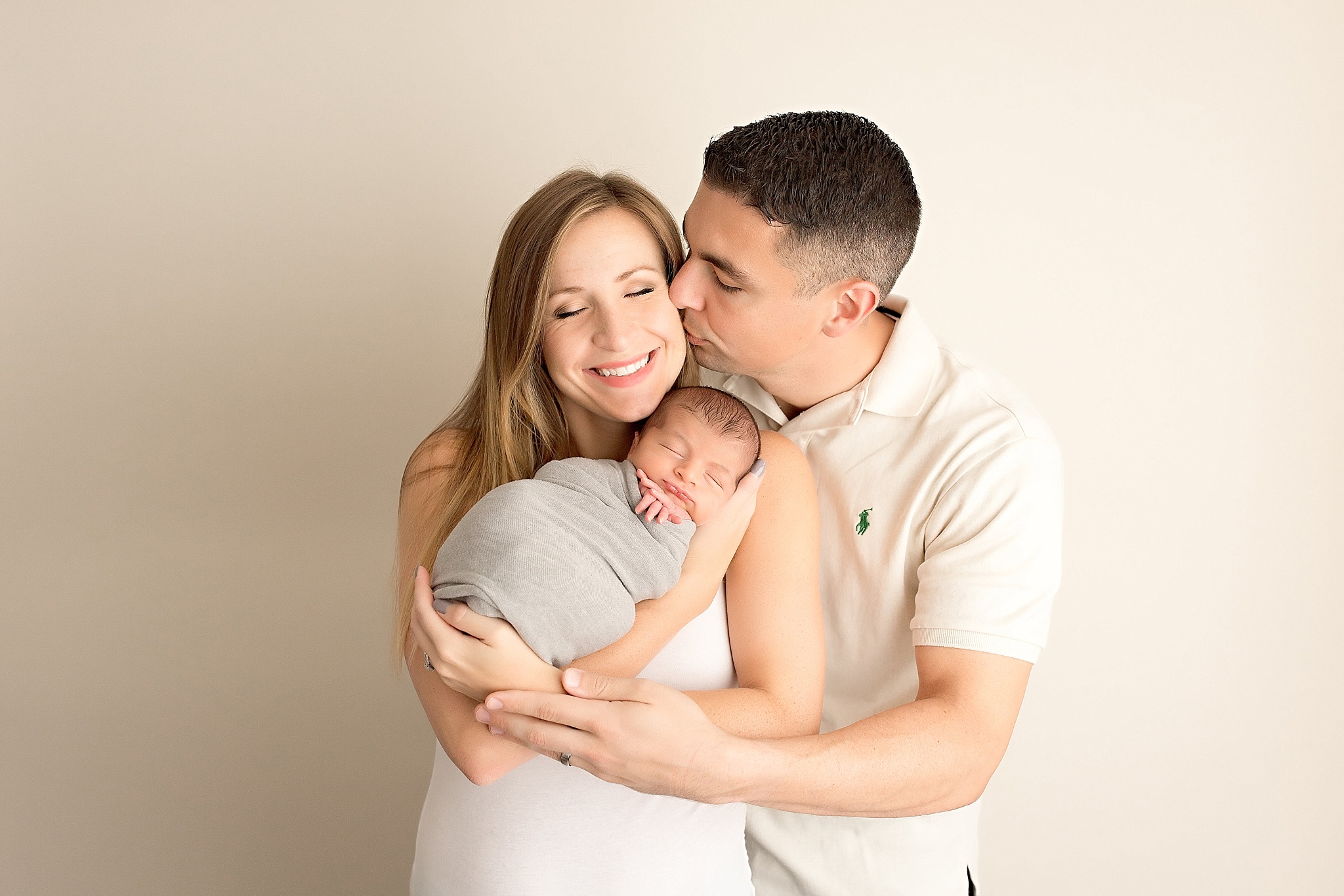 father kissing mother holding newborn baby boy