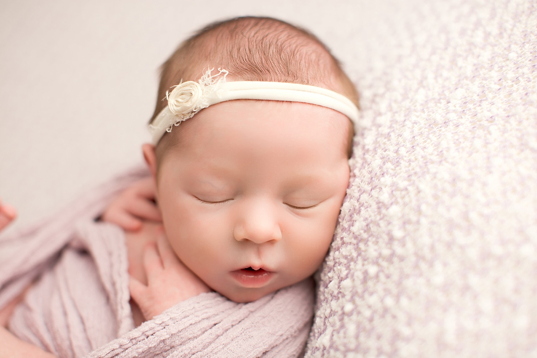 newborn baby girl sleeping in pink wrap with ivory headband
