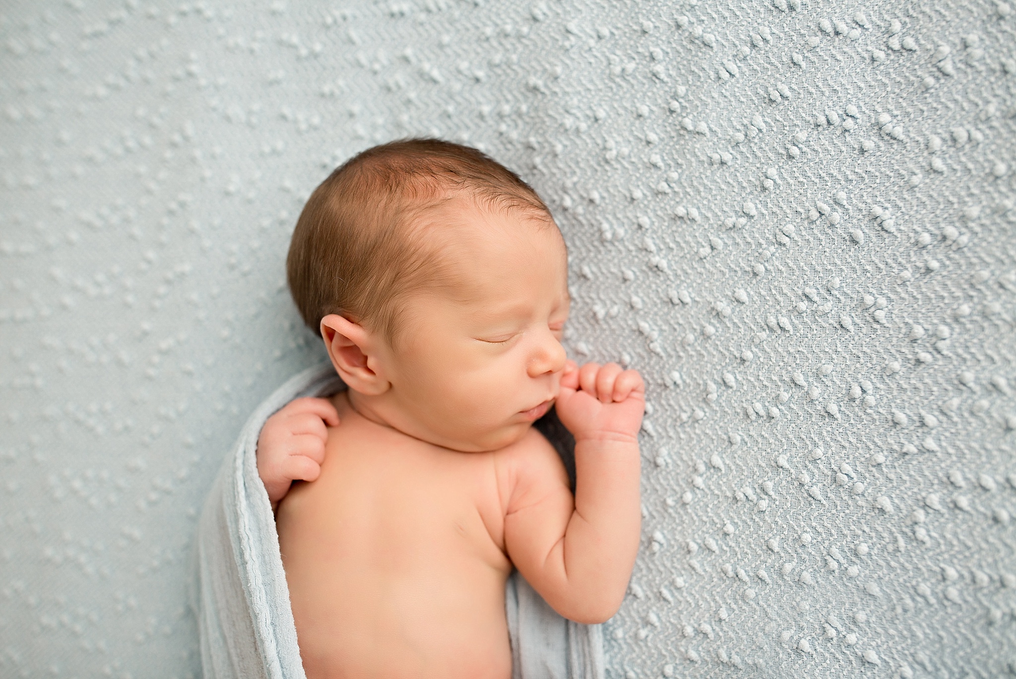 baby sleeping on baby blue sheet during newborn session