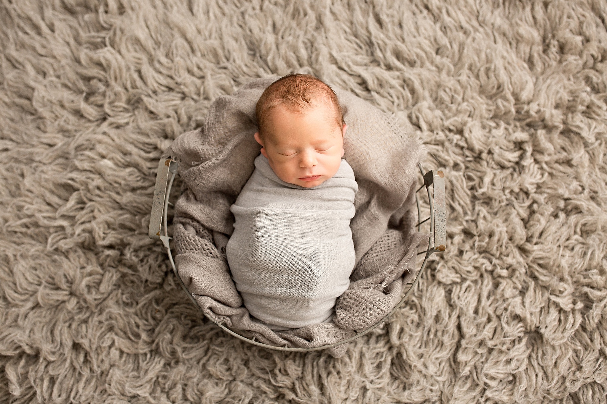 newborn baby boy sleeping on grey basket and blanket during newborn session 