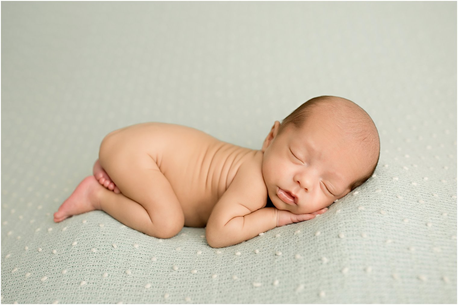 newborn baby boy laying on a mint green blanket