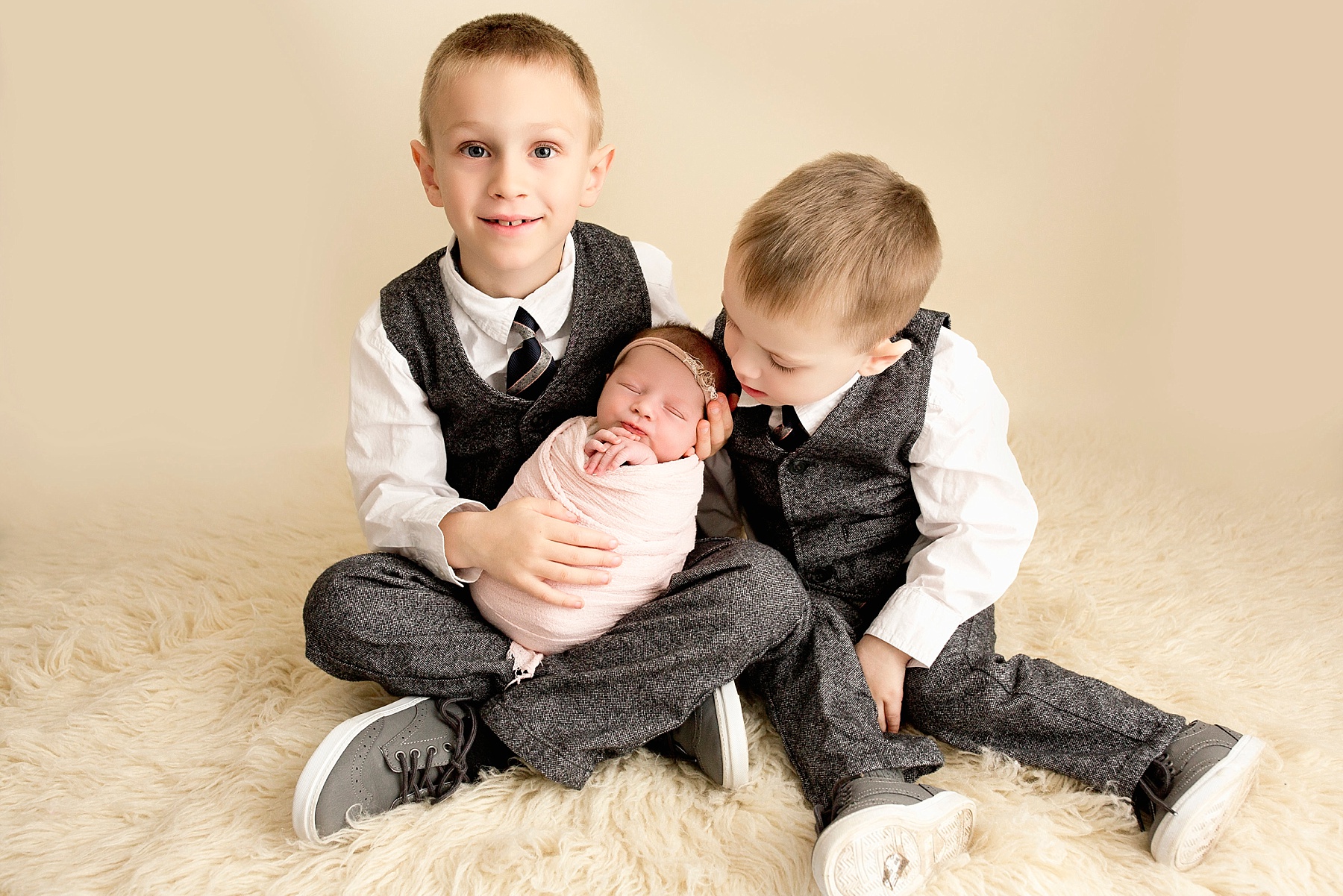 big brother holding newborn baby girl with other brother looking down